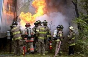 Firefighters use hoses and fire extinguishers to battle the flames engulfing the cab of an 18-wheeler that went off the road and into the woods near the on-ramp from I-110 to I-10 westbound toward Mobile. (Bruce Graner bgraner@pnj.com)